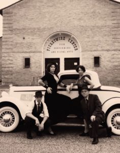 Historic photo of four people posing on 1920s car outside theatre