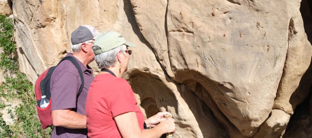 Two hikers looking at drawing of horse on cave wall